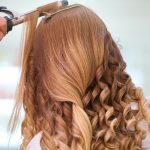 Close-up of a stylist curling blonde hair into glamorous curls at a salon.